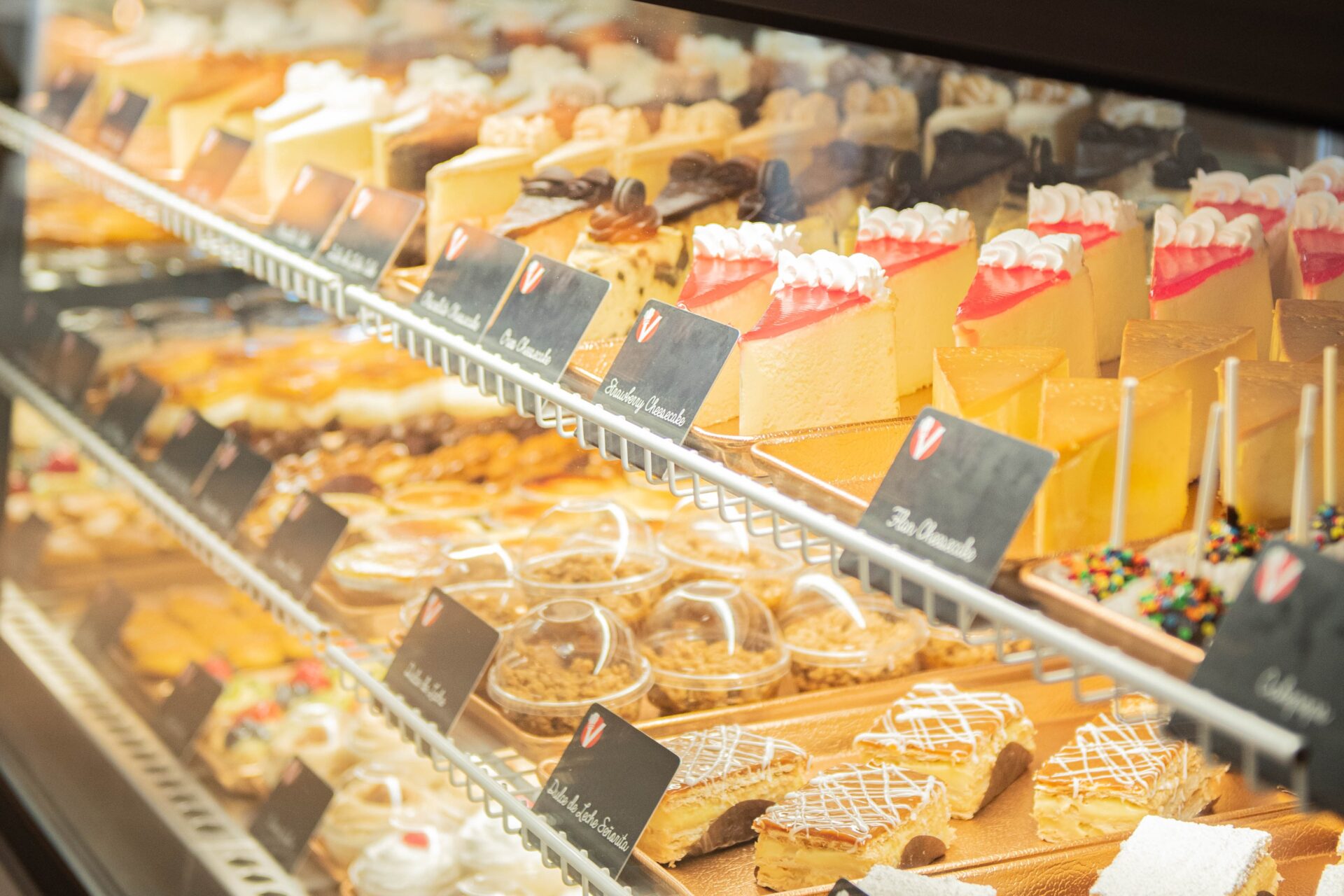 Display case filled with a variety of pastries, cakes, and desserts at Vicky Bakery, including layered sponge cakes with fruit toppings and assorted baked goods
