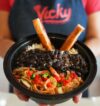 Close-up of a Vicky Bakery employee holding a Platico plate, Cuban food with rice, black beans, shredded meat topped with onions and peppers, and two croquetas